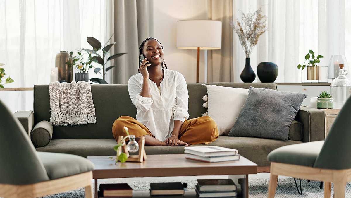 Sunlit Hampton Roads vacation home living room with a smiling woman sitting on a modern green couch talking on the phone, symbolizing stress-free hosting, guest satisfaction, and vacation rental peace of mind